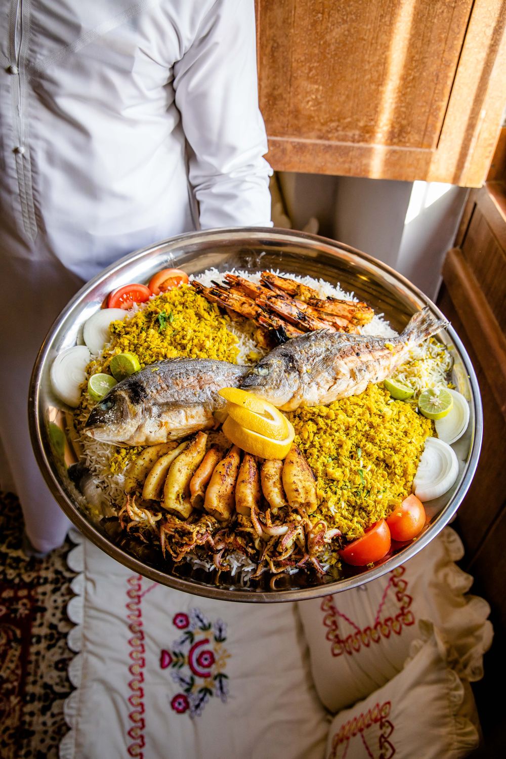 A server holding a seafood tray of grilled fish, prawns and fried fish over spiced rice